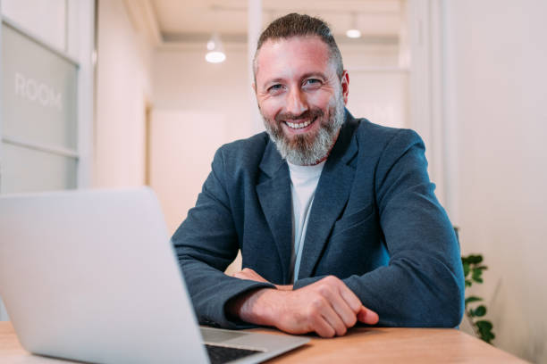 istockphoto-2099549322-612×612 Shot of a businessman sitting on desk in modern office and working on laptop. Portrait of an elegant handsome businessman sitting in his office and using laptop.